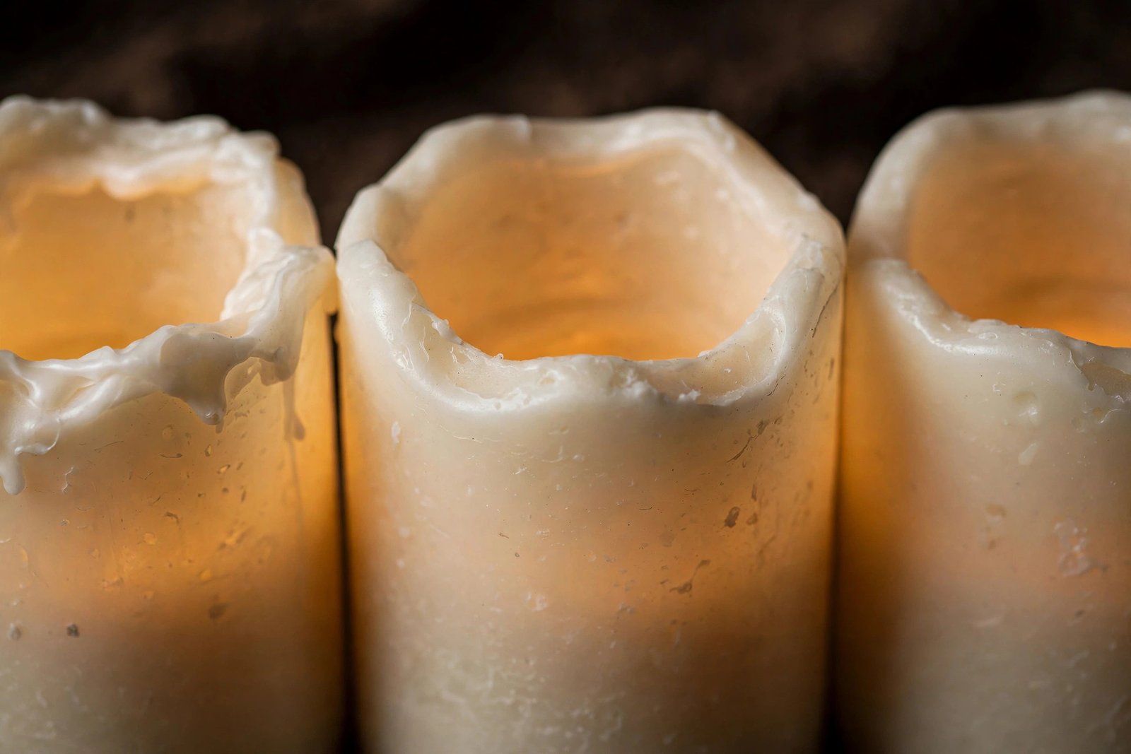 Close-up of ivory real-wax Vinkor flameless pillar candles with wavy melted top rims and warm amber glow